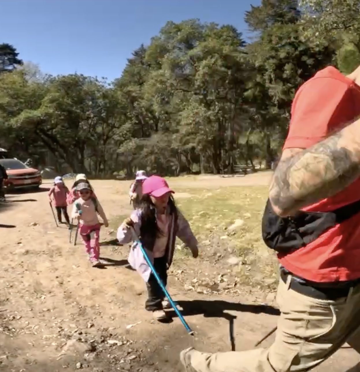 Niñas caminando con bastones de senderismo junto a un guía