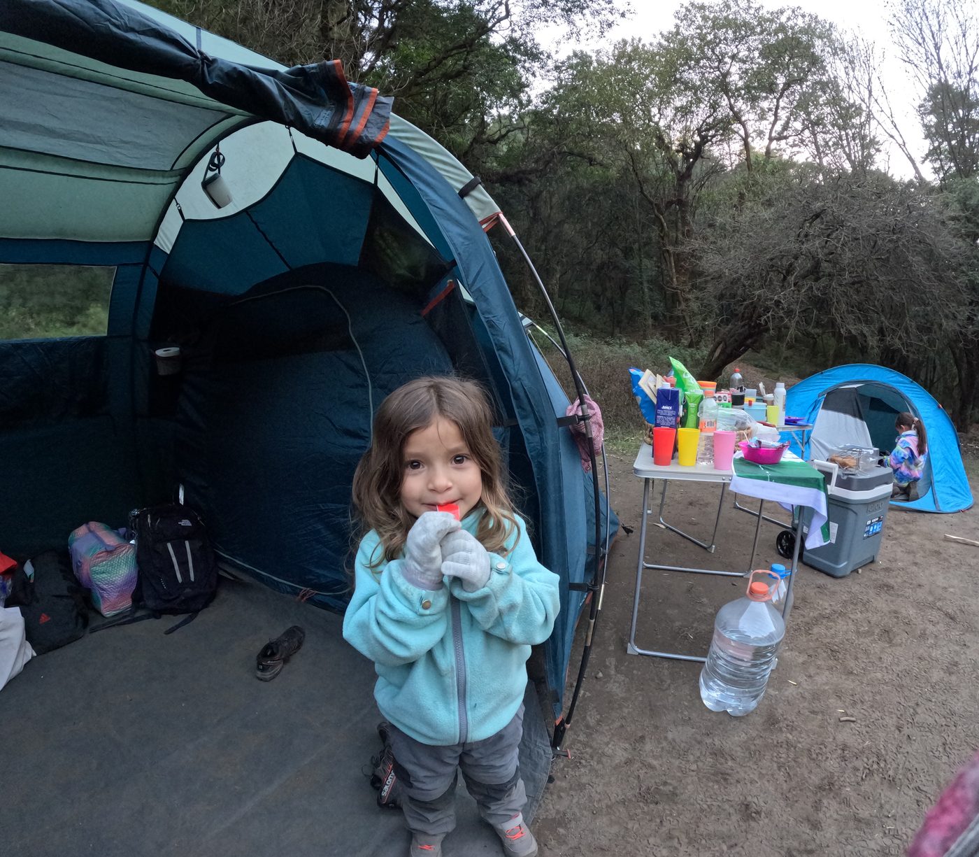 Niña sonriendo frente a su casa de campaña en el campamento