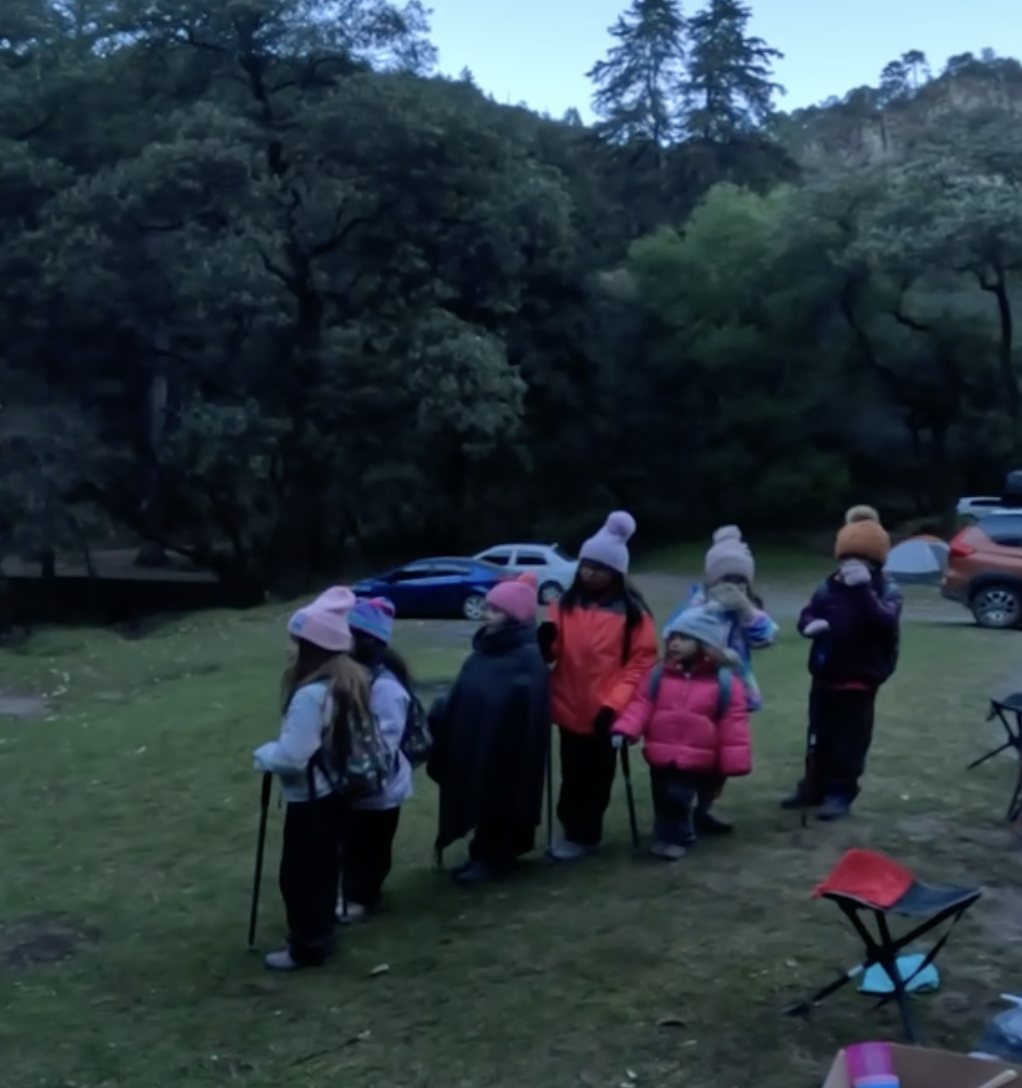Grupo de niñas con bastones y gorros al amanecer en el campamento